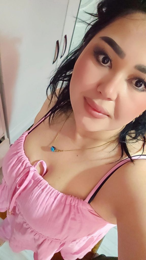 Esmer İzmir escort bayan gülümseyerek iç mekan doğal ışıkta